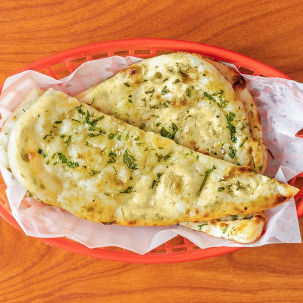 Garlic naan bread, garnished with fresh herbs, served in a red basket lined with white paper.