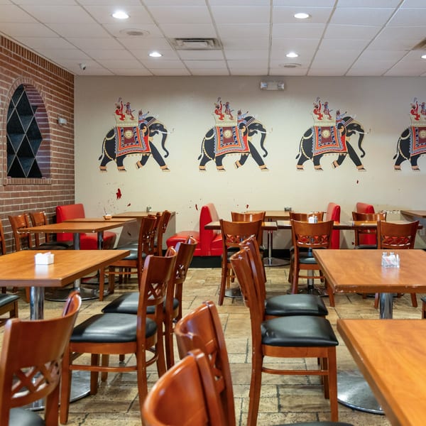 Empty restaurant dining room with wooden tables and chairs, red booths, and elephant murals on the wall.