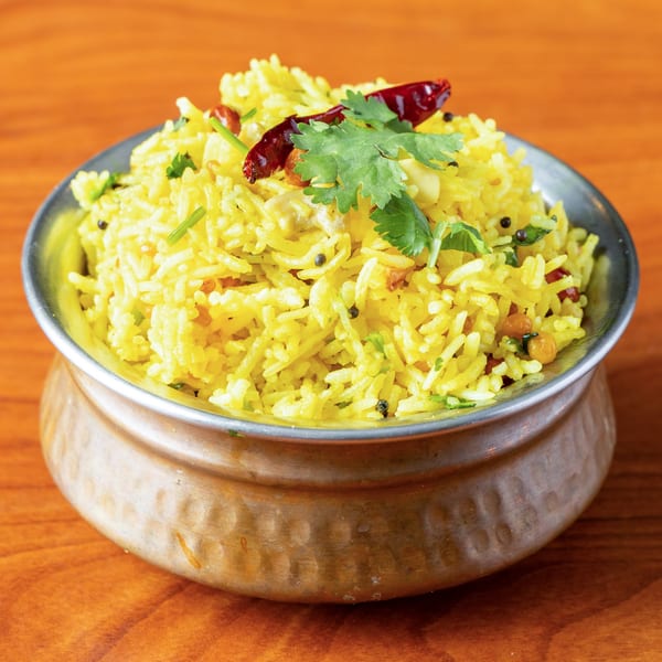 Bright yellow rice with red chilies and green herbs in a hammered metal bowl on a wooden table.