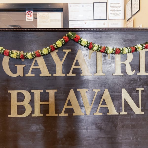 The restaurant name "GAYATRI BHAVAN" in large wooden letters, adorned with a floral garland.