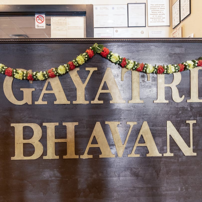 The restaurant name "GAYATRI BHAVAN" in large wooden letters, adorned with a floral garland.