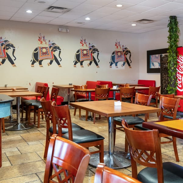 Restaurant dining room with wooden tables and chairs, red booths, and elephant murals on the wall.