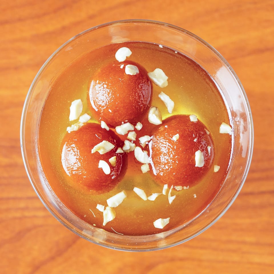 Three gulab jamun, Indian fried dough balls, in syrup and topped with chopped nuts.