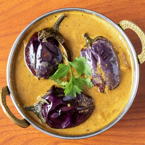 Three purple eggplants in a rich, golden curry sauce, garnished with fresh cilantro in a metal bowl.